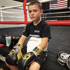 a young boy sitting on the ground wearing boxing gloves