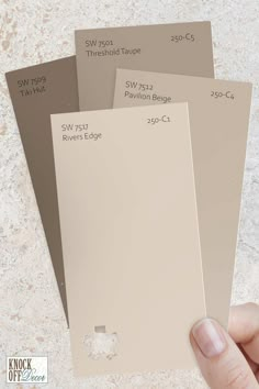 a hand holding three different shades of paint swatches in front of a white background