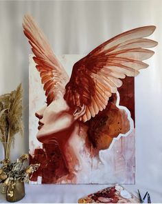 a painting with wings on it next to some dried flowers