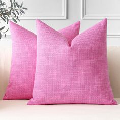 two pink pillows sitting on top of a couch next to a potted green plant