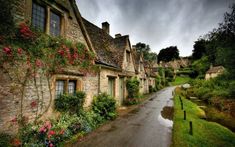 a street lined with stone houses next to lush green bushes and flowers on either side of the road