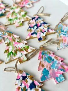 colorful paper christmas trees are hanging from twine ribbons on a white tablecloth with gold trim