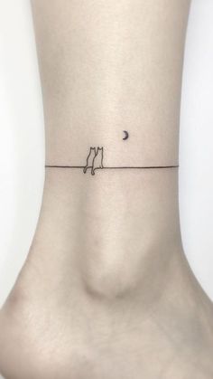 a small tattoo on the ankle of a woman with a cat and moon behind it