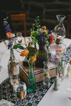 a table topped with lots of vases filled with flowers next to bottles and candles