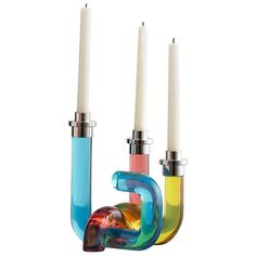 three candles are sitting next to each other in colorful glass holders with one candle sticking out of it