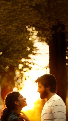 a man and woman standing next to each other in front of a tree at sunset