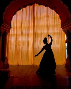 the silhouette of a woman dancing in front of a curtained area with orange drapes