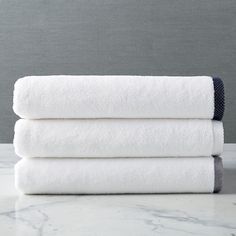 three white towels stacked on top of each other in front of a gray wall and marble countertop