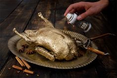 a person is sprinkling seasoning on a roasted chicken in a metal dish