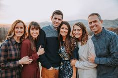 a group of people standing next to each other in front of a mountain range at sunset