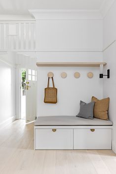 a bench with two pillows on it in front of a white wall and wooden stairs