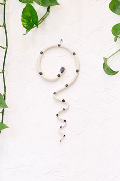 a white and black beaded necklace hanging on a wall next to some green leaves