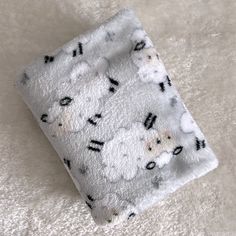 a white fluffy blanket with black and white sheep on it's side, laying on a soft surface