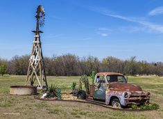 an old rusted truck sitting in the middle of a field next to a windmill