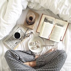 a person laying in bed with an open book and cup of coffee next to them