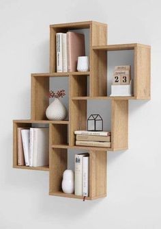 a wooden shelf filled with books on top of a white wall next to a vase