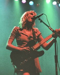 a woman singing into a microphone while holding a guitar in front of a microphone on stage