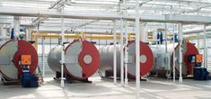 three large tanks in a building with pipes and wires on the ceiling, one is red and white