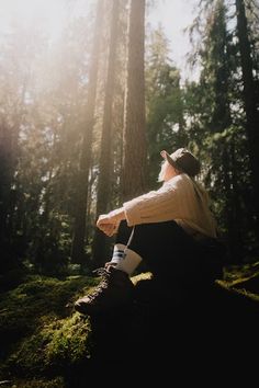 a person sitting on the ground in front of some trees with sun shining through them