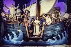 a group of people standing on top of a boat in front of a stage curtain