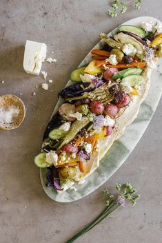 a taco filled with vegetables and cheese on top of a marble slab next to a cup of coffee