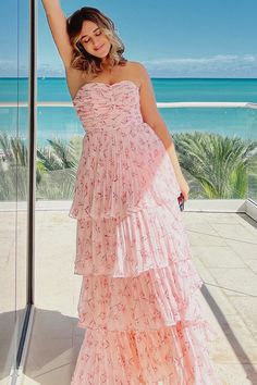 a woman in a pink dress is standing near the ocean and posing for a photo