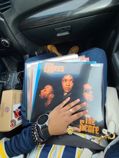 a person sitting in the back seat of a car holding onto some records and a ring