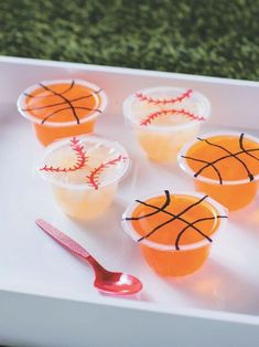 four plastic cups with orange drinks decorated like baseballs on them and a red spoon