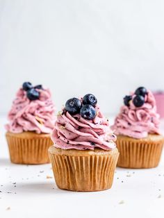 three cupcakes with pink frosting and blueberries on top are sitting in front of each other