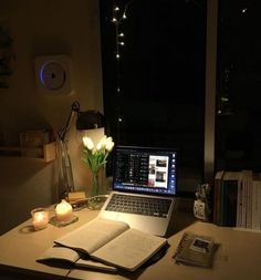 a laptop computer sitting on top of a desk next to an open book and candle