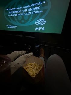 a person sitting in front of a flat screen tv holding a bag of popcorn and watching the movie