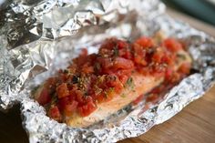 a hot dog covered in tomatoes and seasoning on top of aluminum foil wrapped in foil