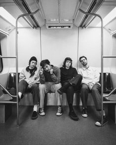 four people sitting on a subway car with their backs to each other and looking at the camera