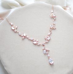 a close up of a necklace on a white cloth with flowers in the background and a rose