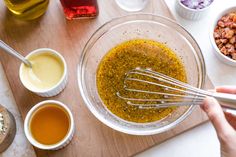 someone mixing ingredients in a glass bowl on a wooden cutting board with utensils