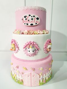 a three tiered cake decorated with pink and white frosting, sheeps and flowers