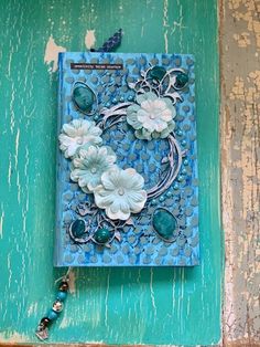 a blue book with white flowers and beads on the cover is sitting on a table