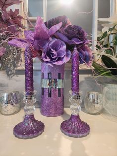 three purple vases with flowers in them on a table