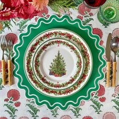 a christmas table setting with plates, silverware and red flowers on the tablecloth