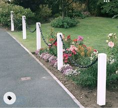 there are many flowers in the garden by the road and fenced off with white posts