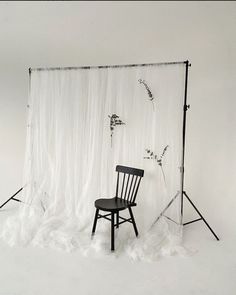 a black chair sitting in front of a white backdrop with flowers on it and an empty chair next to it