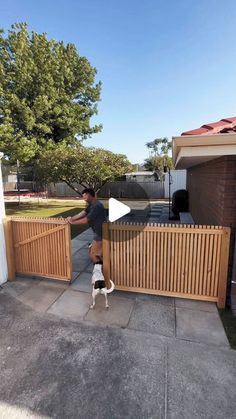 a man standing next to a wooden fence with a dog on the sidewalk behind him