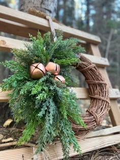 a wreath on a wooden bench with pine cones and evergreen leaves hanging from it's side