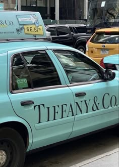 a blue taxi cab parked on the side of a road next to a building with a sign that says tiffany & co