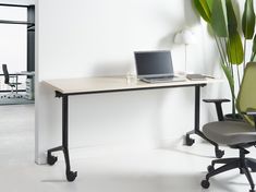 a laptop computer sitting on top of a wooden desk next to a green chair and potted plant