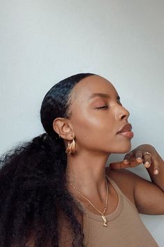 a woman with her eyes closed wearing gold earrings and a brown shirt is leaning against a white wall