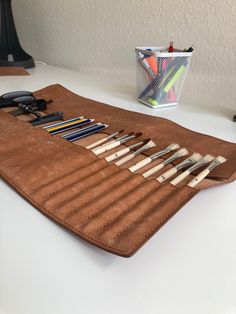 a brown leather case holds several different types of pens and pencils on a white table