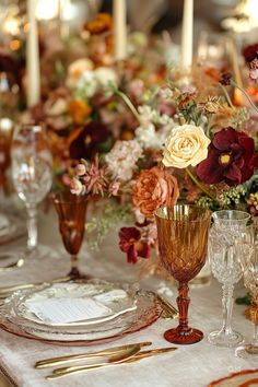 the table is set with gold and red dishes, silverware, and floral centerpieces