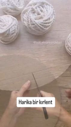 someone is working with yarn on a wooden table while another person holds a pair of scissors