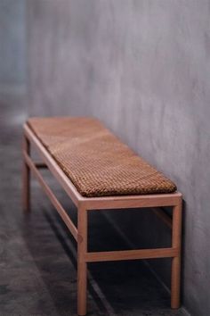 a wooden bench sitting next to a wall with a woven seat cushion on top of it